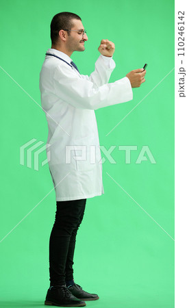 male doctor in a white coat on a green background looking at the phone 110246142