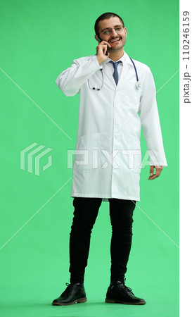 male doctor in a white coat on a green background speaks on the phone 110246159