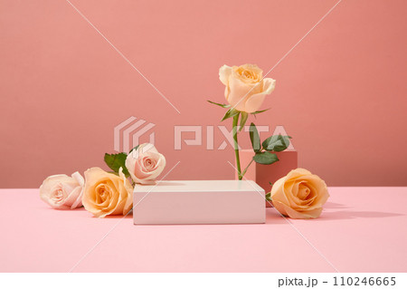 Fresh roses are artistically arranged around the white podium. Ideal space for cosmetics display. Advertising concept with fresh flowers. Front view. Fresh roses are artistically arranged around the white podium. Ideal space for cosmetics display. Advertising concept with fresh flowers. Front view. 110246665