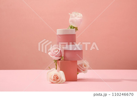 Two unlabeled cosmetic jars are placed on top of each other on a platform with decorative roses. Delicate pink background for cosmetics advertising. Two unlabeled cosmetic jars are placed on top of each other on a platform with decorative roses. Delicate pink background for cosmetics advertising. 110246670