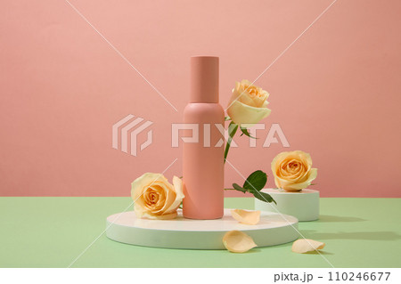 Close up of an unlabeled mineral spray bottle displayed on a white podium against a pink background with fresh roses. Cosmetic advertising space. Close up of an unlabeled mineral spray bottle displayed on a white podium against a pink background with fresh roses. Cosmetic advertising space. 110246677