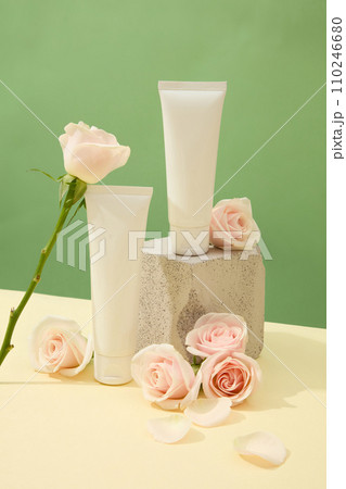 Close-up of two unlabeled cosmetic tubes displayed with fresh roses and a stone platform. Beige surface with pastel green background. Blank label for design. Close-up of two unlabeled cosmetic tubes displayed with fresh roses and a stone platform. Beige surface with pastel green background. Blank label for design. 110246680
