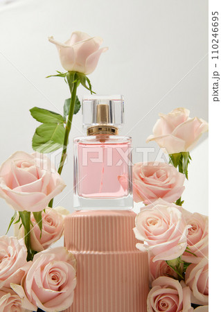 Close-up of an unlabeled perfume bottle displayed on a podium with fresh roses decorated around it. Roses are commonly used in the perfume industry. 110246695