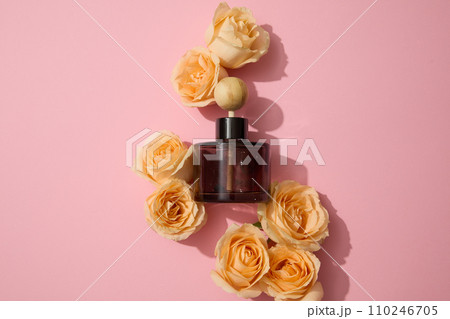 A jar of diffused essential oils stands out among fresh roses on a pink background. Sophisticated and gentle space for advertising. Fragrance from natural ingredients. A jar of diffused essential oils stands out among fresh roses on a pink background. Sophisticated and gentle space for advertising. Fragrance from natural ingredients. 110246705