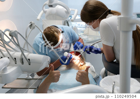 Professional male dentist examining and performing treatment to teenage girl Professional male dentist examining and performing treatment to teenage girl 110249504