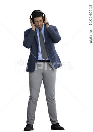 A man in an office suit on a White background listens to music on headphones 110249513