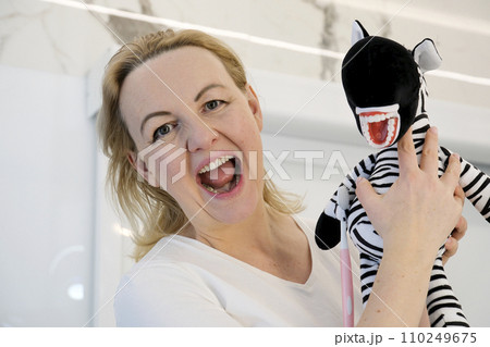 an adult woman in her hands with a toy zebra soft toy striped with real teeth false teeth woman laughs parodying a toy opened her eyes smile joy laughter fun fun dentistry going to the dentist an adult woman in her hands with a toy zebra soft toy striped with real teeth false teeth woman laughs parodying a toy opened her eyes smile joy laughter fun fun dentistry going to the dentist 110249675