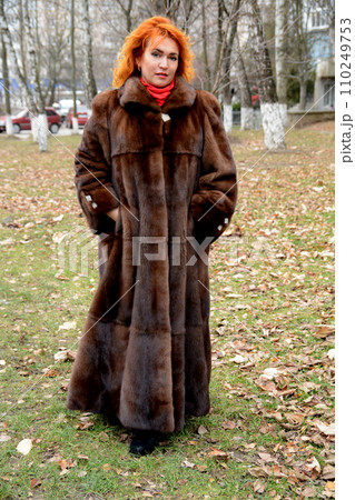 red-haired beautiful middle-aged woman in a long fur coat in the park forest on the street walks looks into the frame red scarf bright brown mink coat red-haired beautiful middle-aged woman in a long fur coat in the park forest on the street walks looks into the frame red scarf bright brown mink coat 110249753