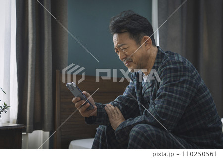 スマートフォンを見ながら顔をしかめる中年男性 110250561