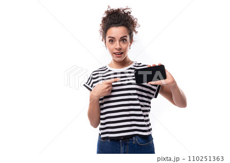 young caucasian woman with a curly haircut dressed in a striped summer t-shirt shows the smartphone young caucasian woman with a curly haircut dressed in a striped summer t-shirt shows the smartphone 110251363