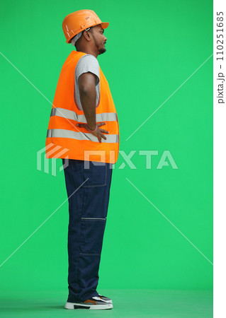 A male construction worker, on a green background, holds his hands on his belt, in profile A male construction worker, on a green background, holds his hands on his belt, in profile 110251685