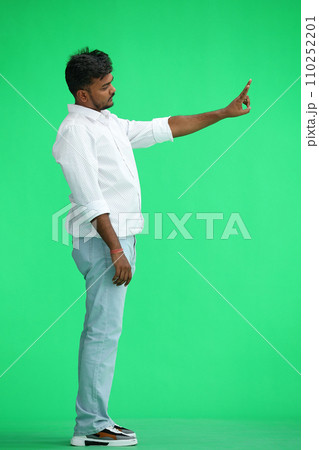 A man in a white shirt, on a green background, in full height, shows a victory sign, profile A man in a white shirt, on a green background, in full height, shows a victory sign, profile 110252201