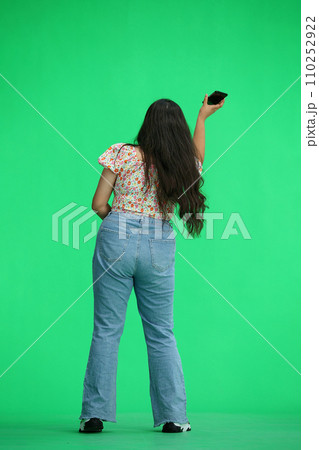 A woman, on a green background, in full height, waving his phone, back view 110252922