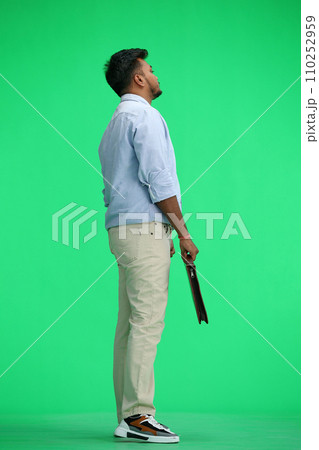A man in a blue shirt, on a green background, full-length, with a briefcase in his hands, in profile 110252959