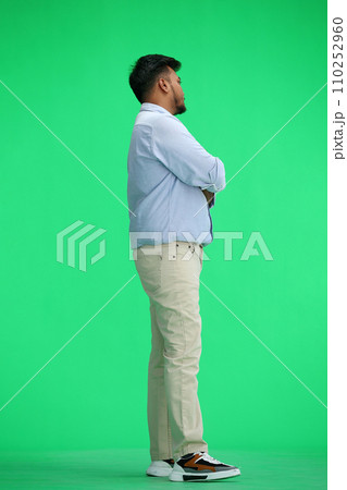 A man in a blue shirt, on a green background, in full height, crossed his arms, in profile 110252960