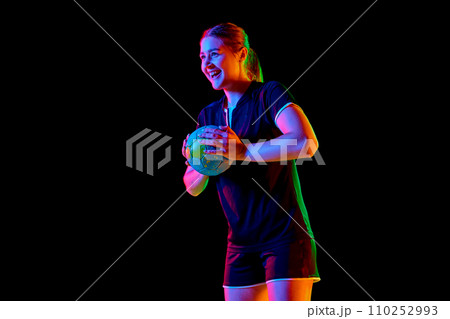 Portrait of young woman, handball player holding ball to make perfect precise serve early in game against black background in neon light. 110252993