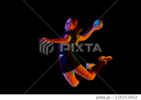 Fit, young, competitive female handball player demonstrating throwing techniques against black background in neon light. Concept of championship 2024. 110253002