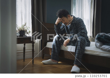 ベッドに座って頭を抱える50代の男性 110253701