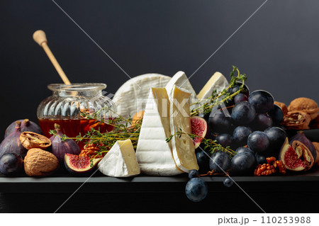 Camembert cheese with fruits and honey on a black background. Camembert cheese with fruits and honey on a black background. 110253988