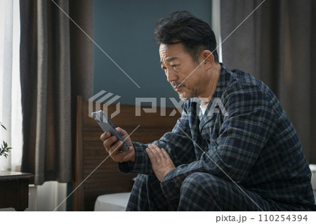 暗い表情でスマホを見る中年男性 110254394