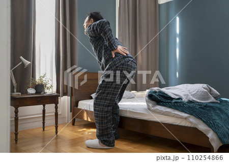 ベッドのそばで腰に手をあてるパジャマ姿の中高年男性 110254866