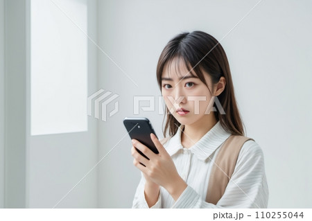 スマートフォンを手に持って怒り気味に驚く日本人美女 110255044