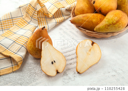 Whole and halves of pears, wicker basket and yellow kitchen towel on white wooden background.. 110255428