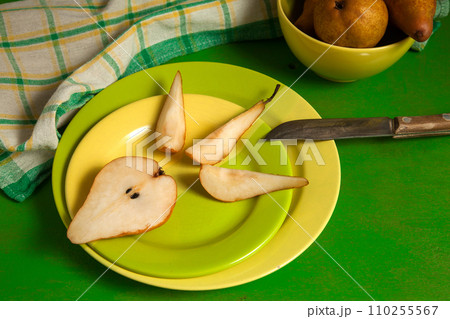 Green plate with slices and half of pear and green kitchen towel on green wooden background.. Green plate with slices and half of pear and green kitchen towel on green wooden background.. 110255567