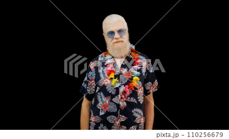 Positive mature man in a Hawaiian shirt stands against a black background, radiating happiness like a joyful tourist Positive mature man in a Hawaiian shirt stands against a black background, radiating happiness like a joyful tourist 110256679