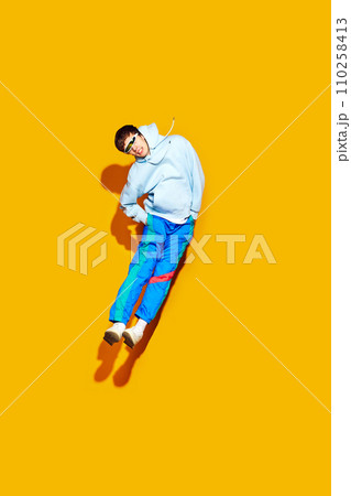 Full length portrait of man in trendy sportswear jumps against yellow background, showing perfect combination of fashion and energy. 110258413
