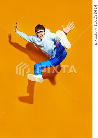 Full length portrait of young man dressed in the latest fashion jumps on a bright yellow background, realizing fusion of style and movement. Full length portrait of young man dressed in the latest fashion jumps on a bright yellow background, realizing fusion of style and movement. 110258414