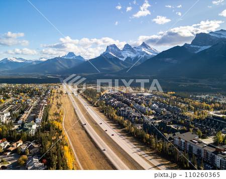 Canmore, Alberta, Canada. Aerial view of Trans-Canada Highway (Highway 1) in a autumn sunny day. The Three Sisters trio of peaks Canadian Rockies mountain range. Canmore, Alberta, Canada. Aerial view of Trans-Canada Highway (Highway 1) in a autumn sunny day. The Three Sisters trio of peaks Canadian Rockies mountain range. 110260365