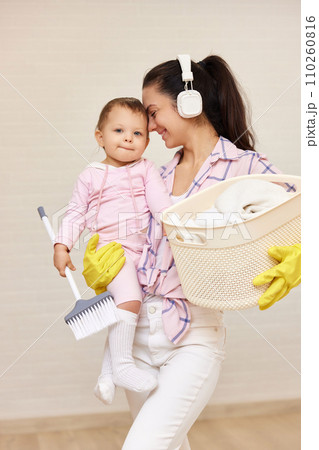 happy mother housewife is holding cute little child girl and basket with laundry and doing housework , Happy family happy mother housewife is holding cute little child girl and basket with laundry and doing housework , Happy family 110260816