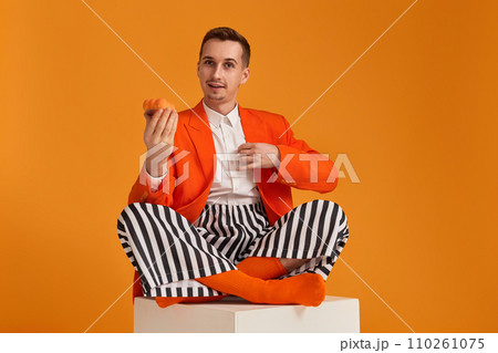 extravagant funny young man in orange jacket and striped pants holding cupcake on orange background. 110261075