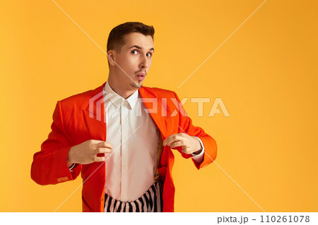 Cheerful funny young man in orange jacket and striped pants on yellow background. Cheerful funny young man in orange jacket and striped pants on yellow background. 110261078