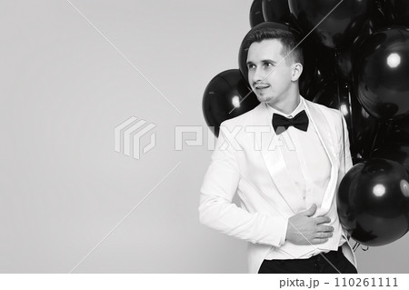 elegant man in white suit tuxedo with black air balloons. copy space. holiday celebration elegant man in white suit tuxedo with black air balloons. copy space. holiday celebration 110261111