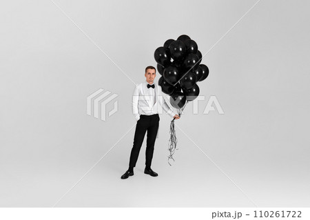 elegant caucasian man in white suit tuxedo with black air balloons on white background. Full length. birthday party elegant caucasian man in white suit tuxedo with black air balloons on white background. Full length. birthday party 110261722