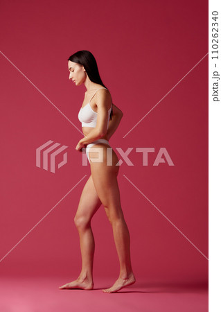 Full-length of young brunette woman with slim, fit, healthy body standing in white cotton underwear against pink studio background Full-length of young brunette woman with slim, fit, healthy body standing in white cotton underwear against pink studio background 110262340