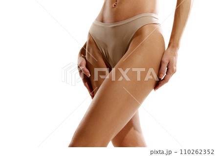 Cropped image of tanned female legs, buttocks in beige cotton underwear against white studio background Cropped image of tanned female legs, buttocks in beige cotton underwear against white studio background 110262352