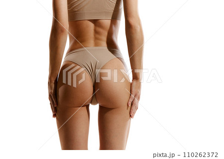 Cropped back view image of slim female body, buttocks in beige cotton underwear against white studio background. Anti-cellulite care, massage 110262372