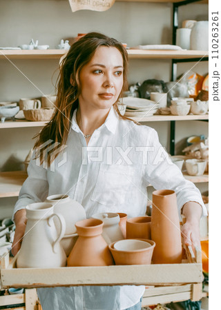 Beautiful middle-aged woman with various pottery items in a box. A young woman presents clay products in her shop-workshop, a creative small business 110263261
