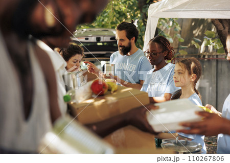 African American and Caucasian individuals distribute food and supplies to needy. Volunteers share boxes filled with canned goods and meal boxes spreading joy and helping combat poverty and hunger. 110267806