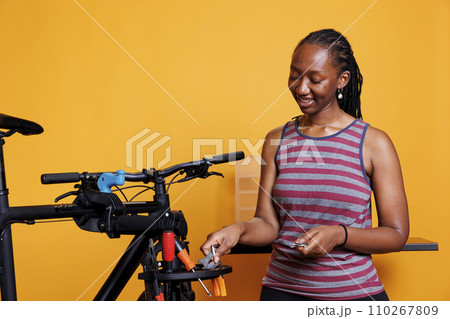Dedicated black woman selects and examines several equipment from a professional toolkit for bike repair. Active african american lady clutching and arranging specialized bicycle maintenance tools. Dedicated black woman selects and examines several equipment from a professional toolkit for bike repair. Active african american lady clutching and arranging specialized bicycle maintenance tools. 110267809