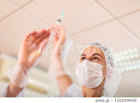 Nurse or doctor wearing in face mask and medical uniform holding vial and syringe Nurse or doctor wearing in face mask and medical uniform holding vial and syringe 110269600