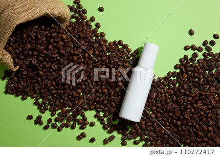 Creative background for advertising with white empty bottle displayed on coffee beans and green background. Top view. Coffee contains antioxidants that can help protect against UV ray Creative background for advertising with white empty bottle displayed on coffee beans and green background. Top view. Coffee contains antioxidants that can help protect against UV ray 110272417
