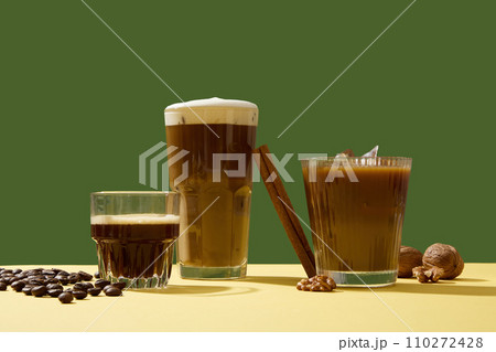Different delicious cups of coffee with creamy foam decorated on a green background with coffee beans, cinnamon sticks and walnuts. A cup of coffee in the morning helps you feel more alert and active Different delicious cups of coffee with creamy foam decorated on a green background with coffee beans, cinnamon sticks and walnuts. A cup of coffee in the morning helps you feel more alert and active 110272428