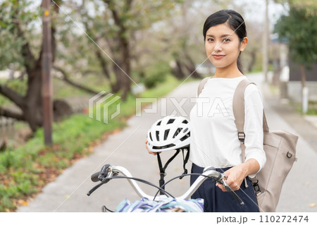 ヘルメットを抱えて自転車の横に立つ若い女性 110272474