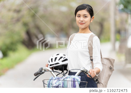ヘルメットを抱えて自転車の横に立つ若い女性 110272475