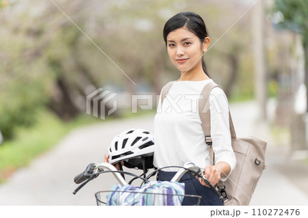ヘルメットを抱えて自転車の横に立つ若い女性 110272476