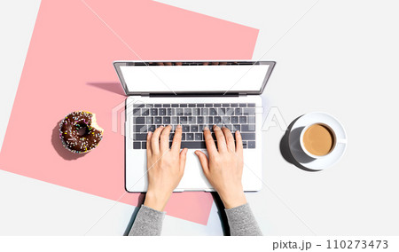 Person using a laptop computer with a donut and a cup of coffee Person using a laptop computer with a donut and a cup of coffee 110273473